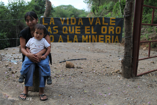 This photo shows Angelina Noj from San Pedro Ayampuc in Guatemala holding her small son Esmit in front of the blocked entrance gate to the Tambor gold mine. Photo: James Rodríguez