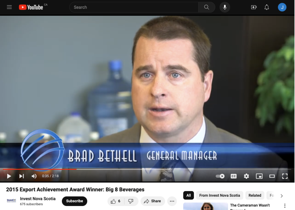 The face of a clean-shaven man with short-cropped brown hair and blue eyes in the foreground, with a large plastic bottle of water with a blue tint and cap behind him, and under his face, a blue circle logo with three curved lines inside it, and the words 'Brad Bethell, General Manager" in a blue banner across the bottom of the screenshot, taken from a video.